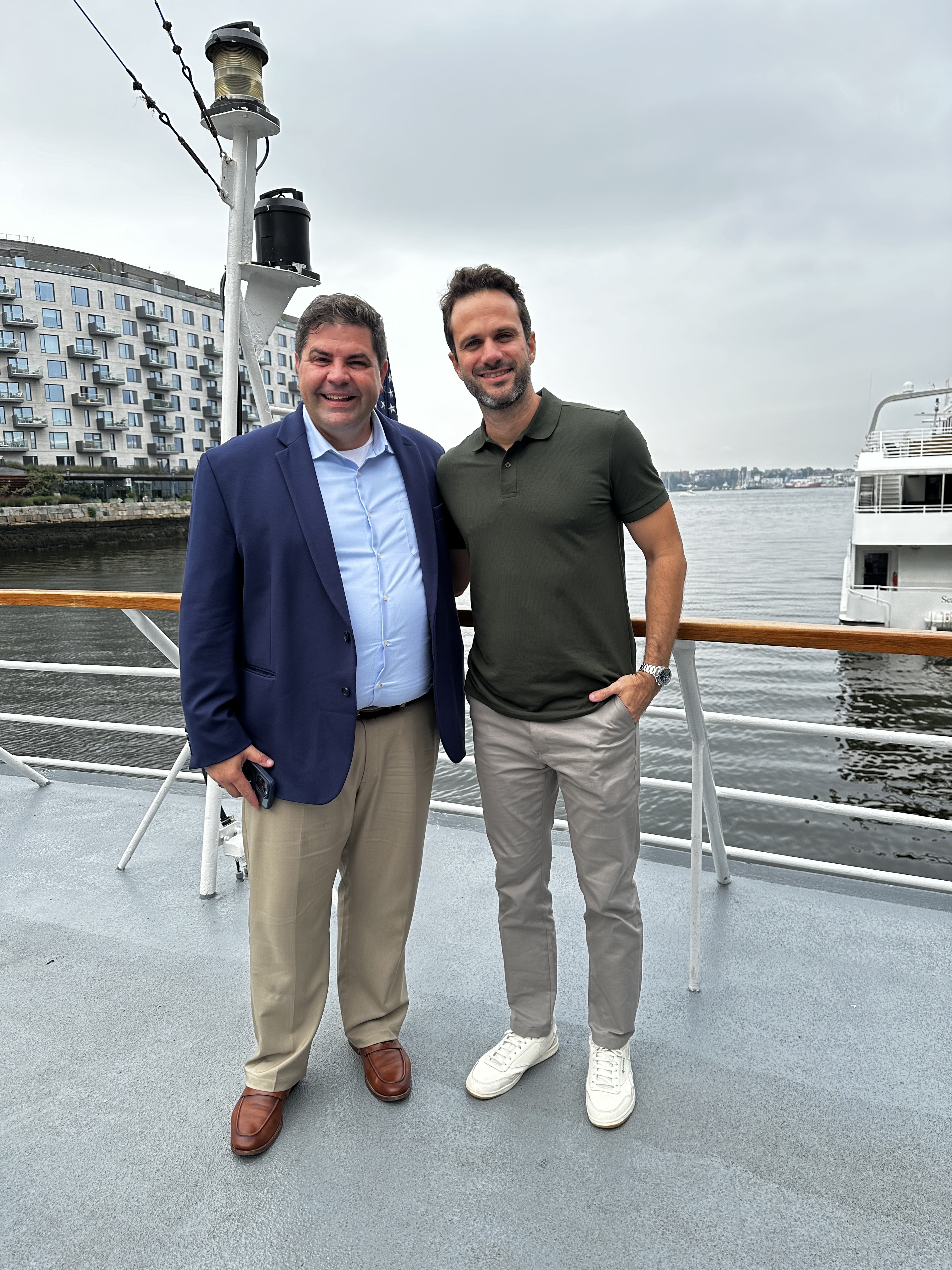 Thiago Lago com convidado a bordo de embarcação, com paisagem urbana ao fundo.