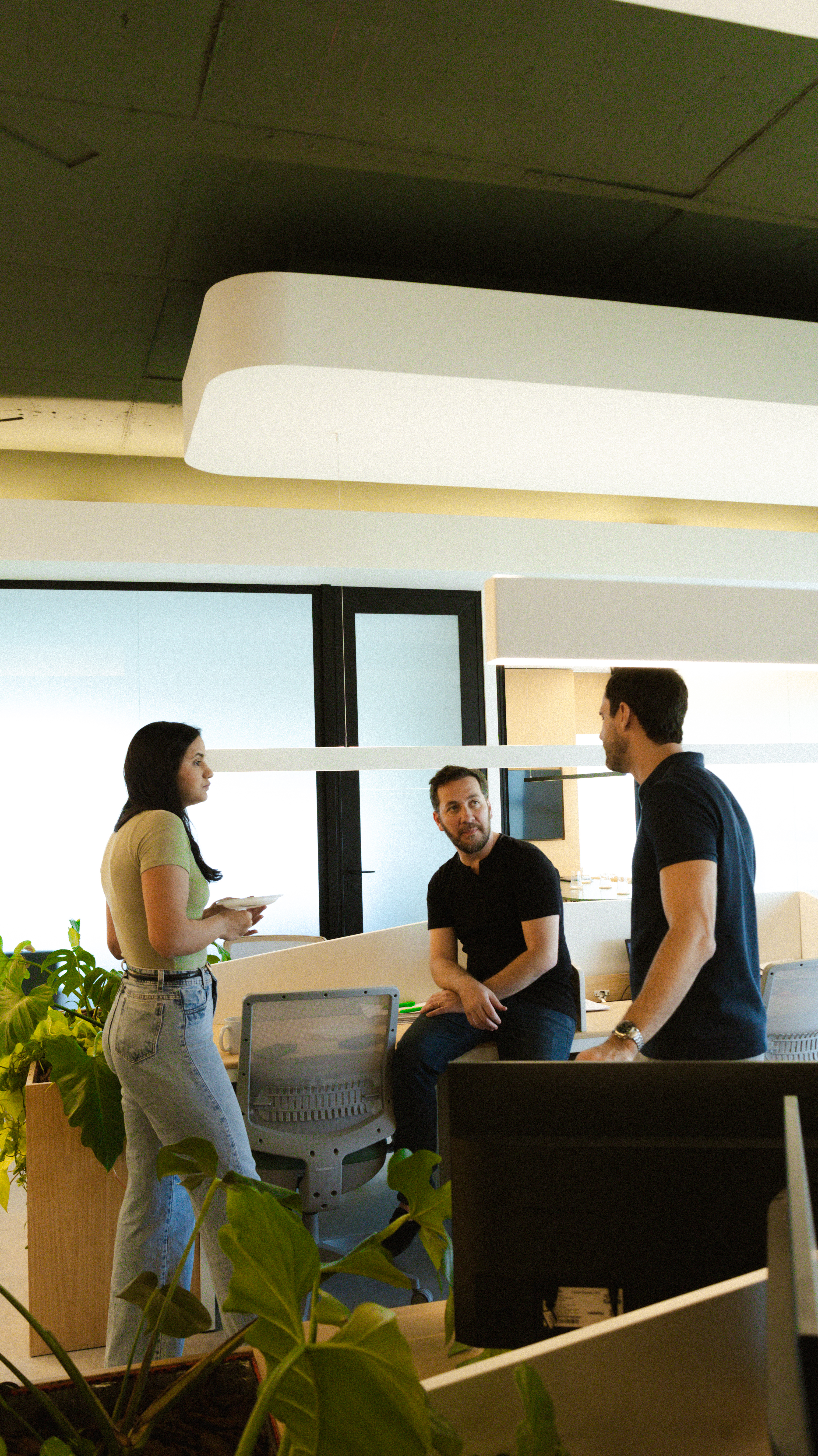 Thiago Lago em conversa com dois colegas em ambiente de coworking moderno.